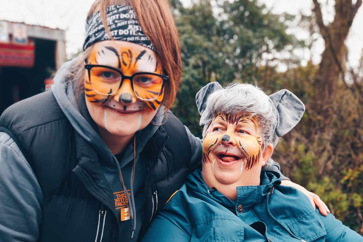 Two ladies smiling with faces painted as tigers