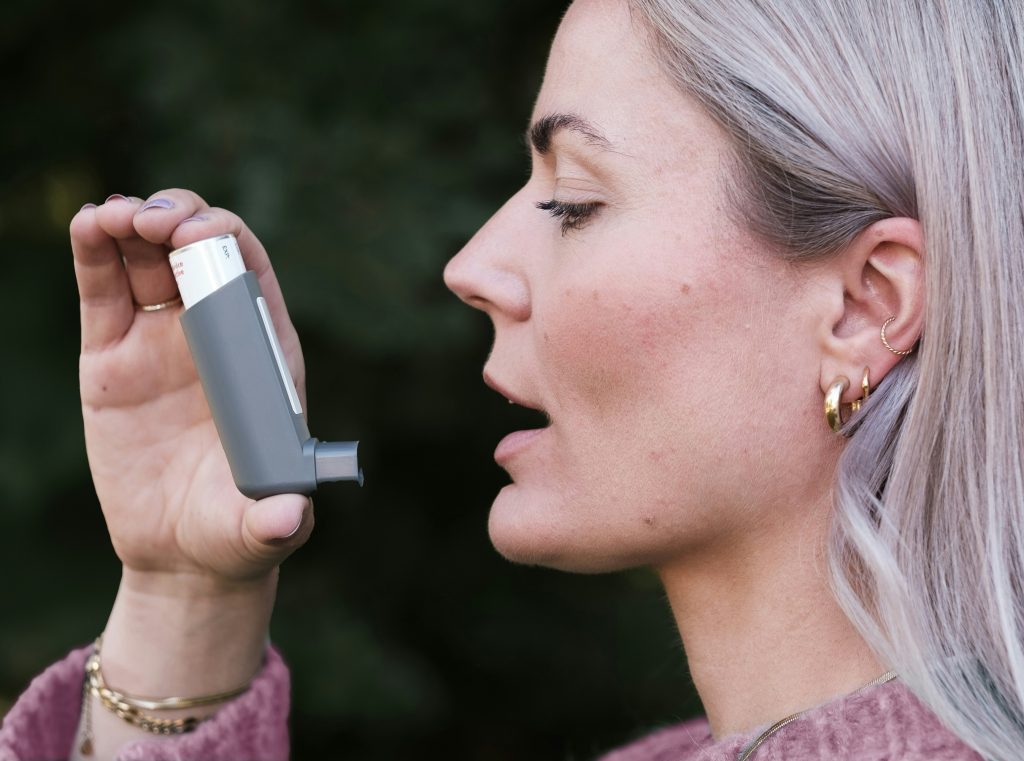 Woman with asthma using an inhaler to aid her long-term health condition.